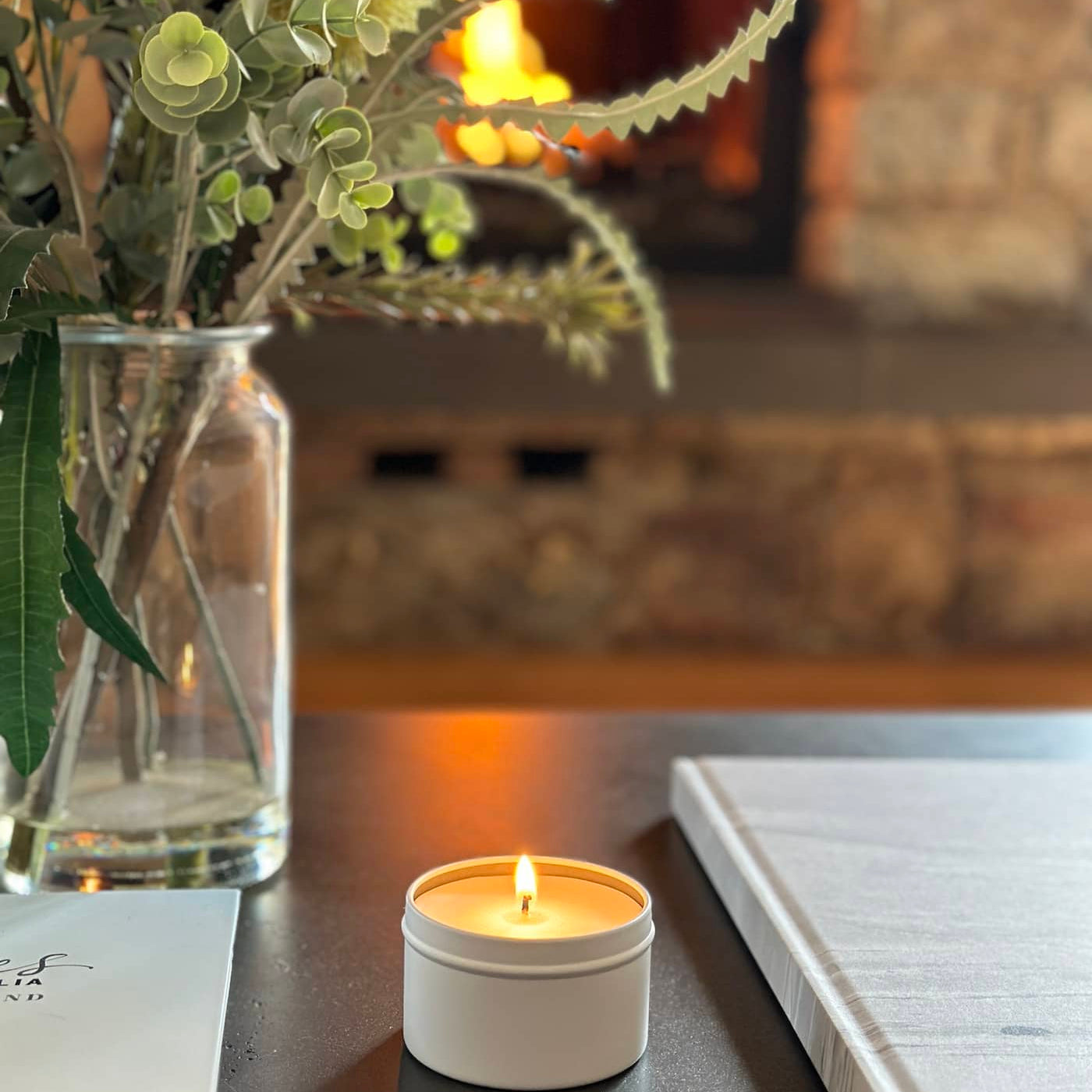 Caitlin Louise Collection Travel Tin Candle on coffee table - fire burning in fireplace in background