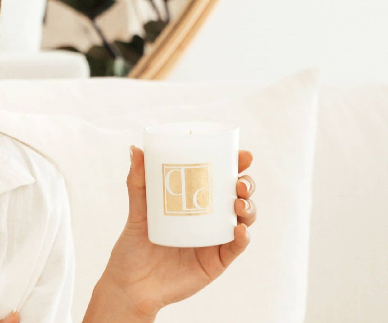 Caitlin Louise Collection Signature Collection Scented Candle - held in model's hand - white lounge in background
