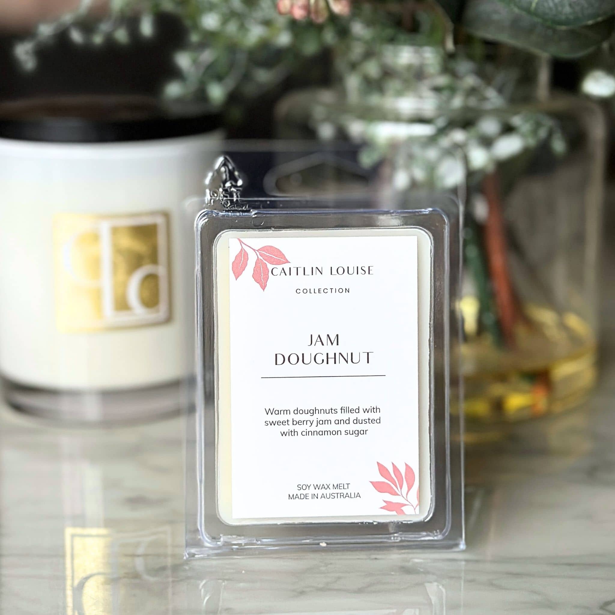 Caitlin Louise Collection wax melt labeled 'Jam Doughnut' in front of a candle.