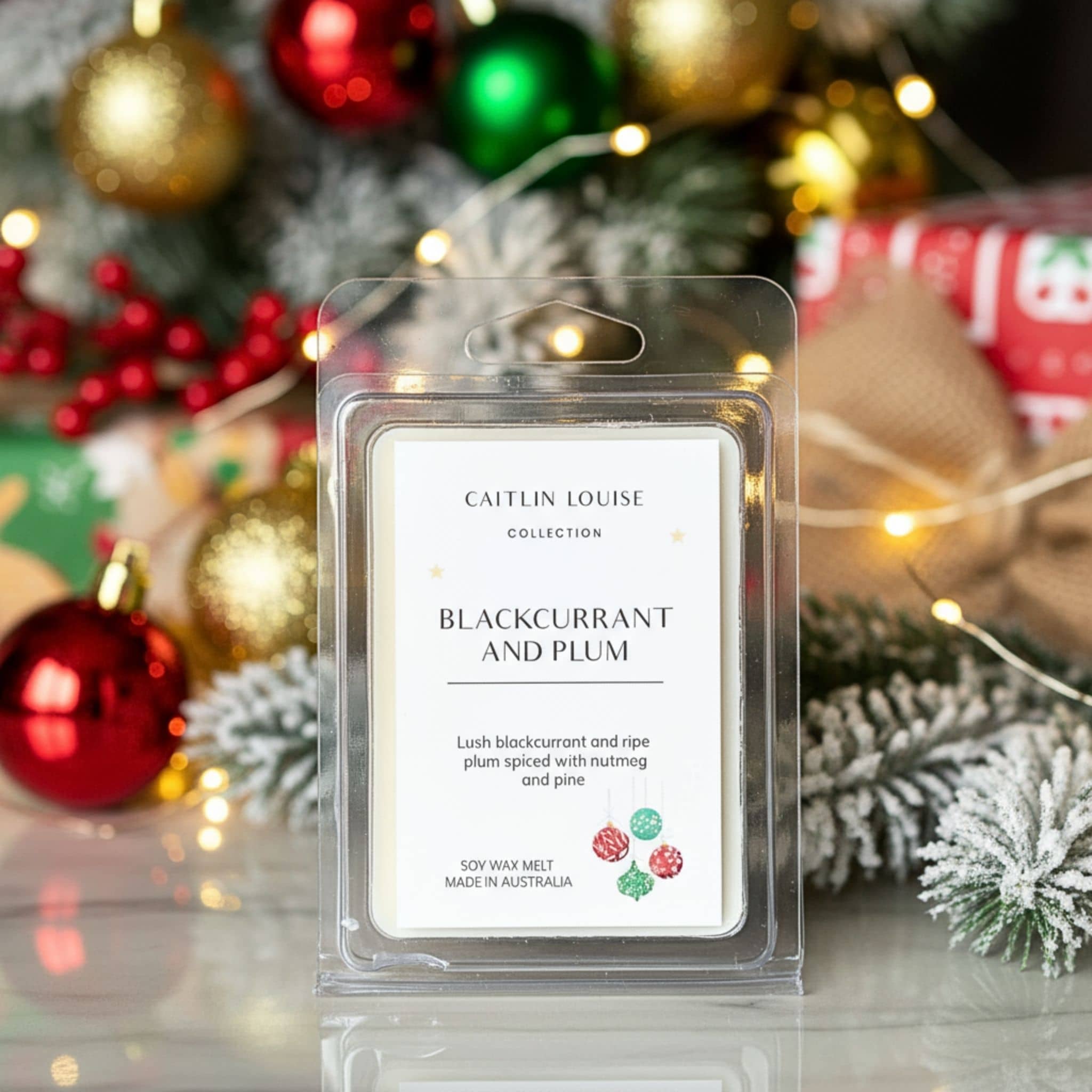 Caitlin Louise Blackcurrant and Plum wax melt packaging with Christmas decorations in the background