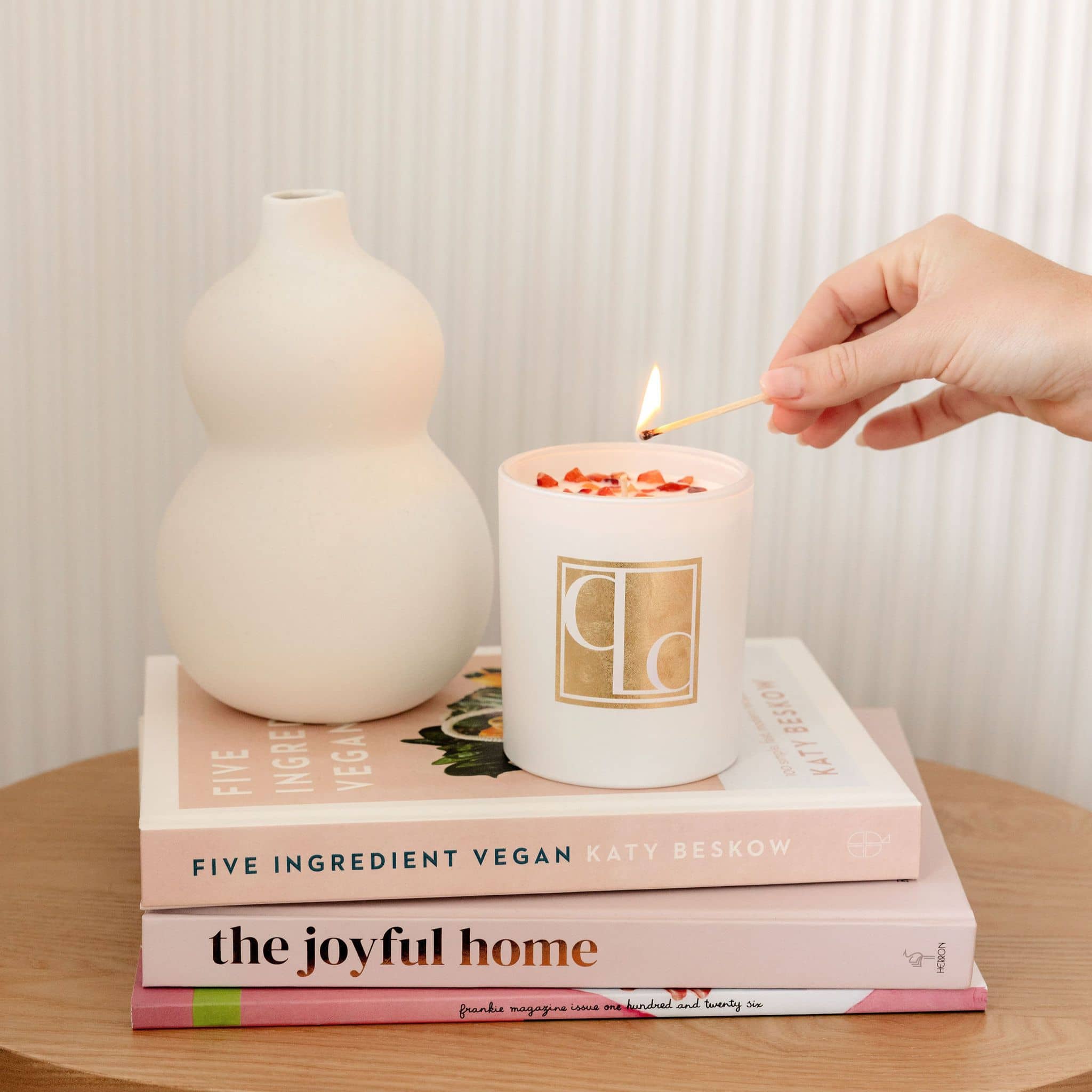 Champagne Sunset crystal infused candle on stack of books - hand holding lit match to light the wick