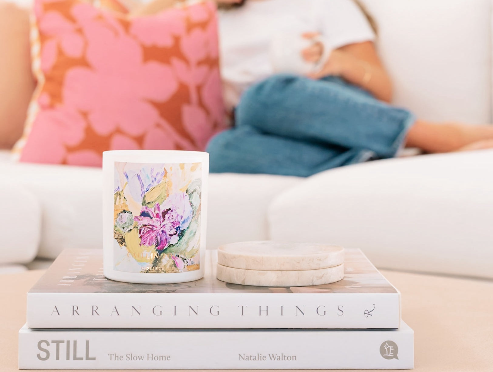 Patchouli and Sandalwood Scented Artist Candle - styled on books and coffee table with lady sitting on the lounge in the background