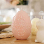 Decorative pink egg-shaped candle on a wooden surface with blurred background
