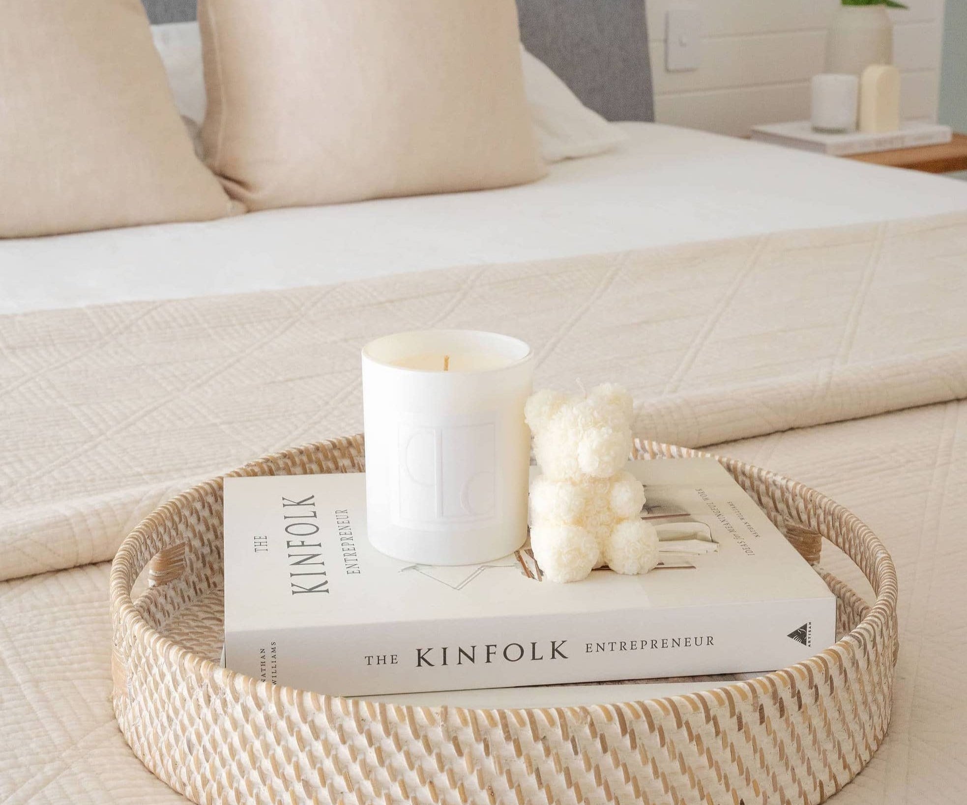 Caitlin Louise Collection salty caramel kiss soy candle styled with Aria sculptural candle on a book and tray - on a bed in a beautiful bedroom.