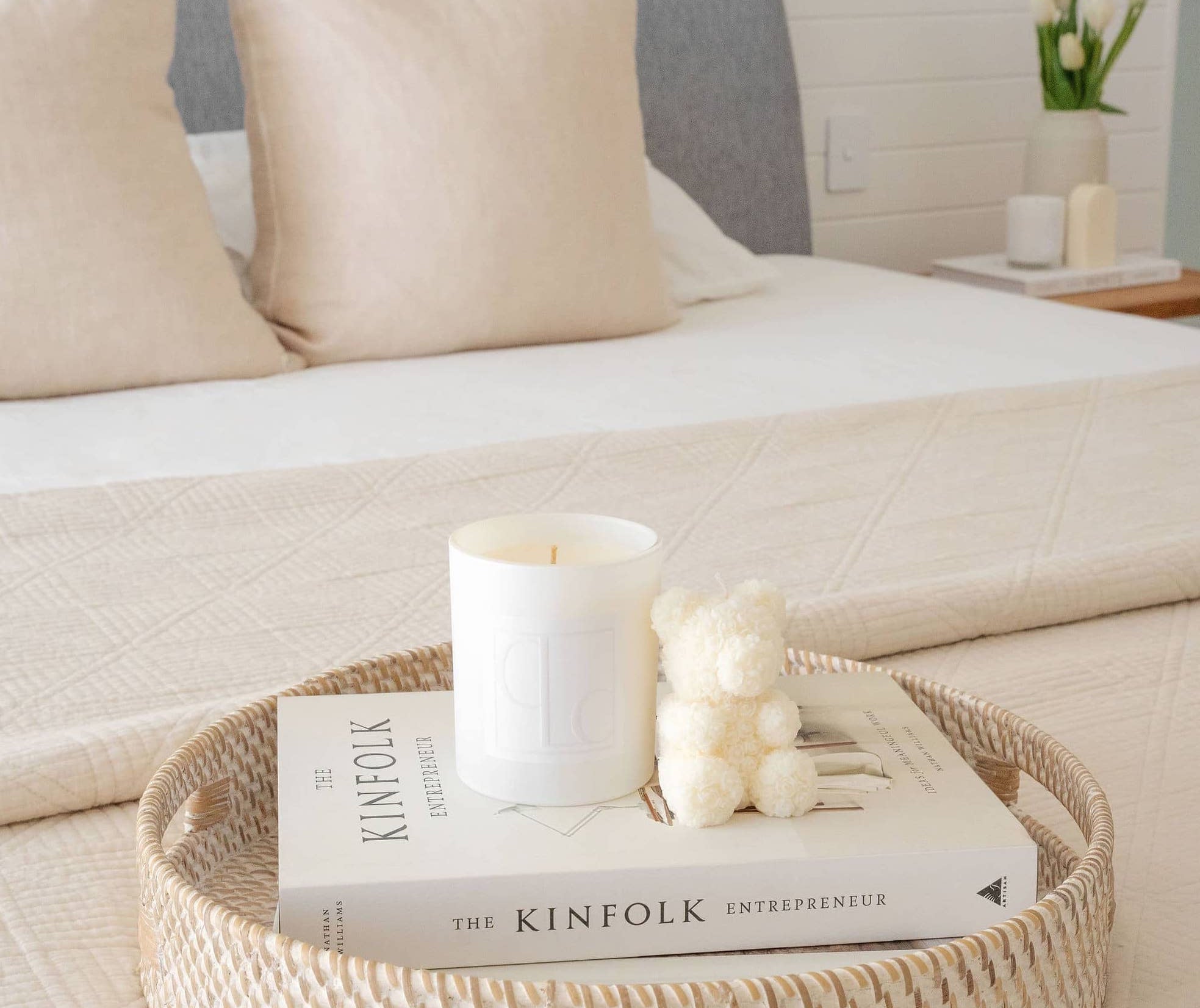 Caitlin Louise Collection salty caramel kiss soy candle styled with Aria sculptural candle on a book and tray - on a bed in a beautiful bedroom.