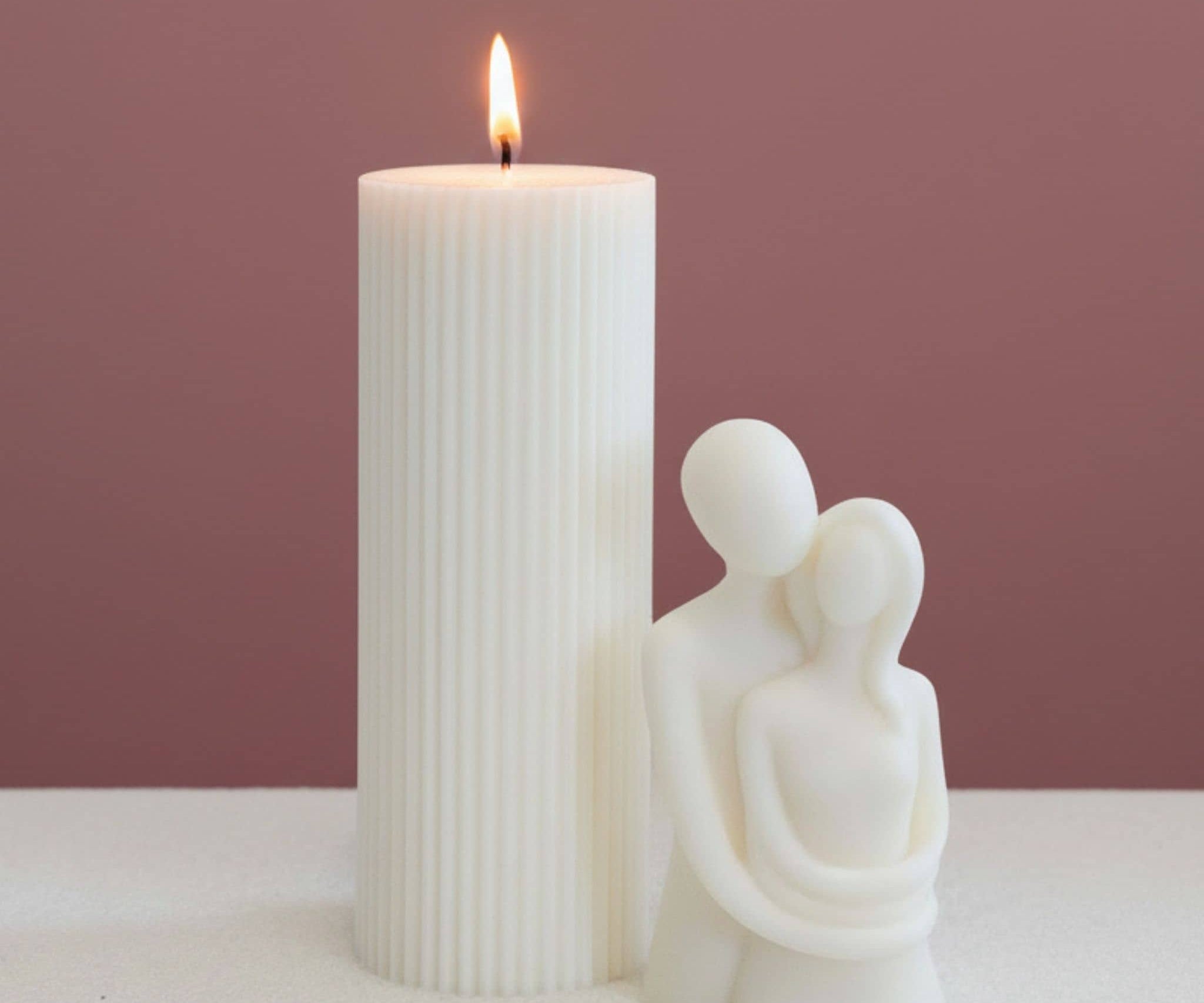 Two sculptural candles with a dark pink background and white base