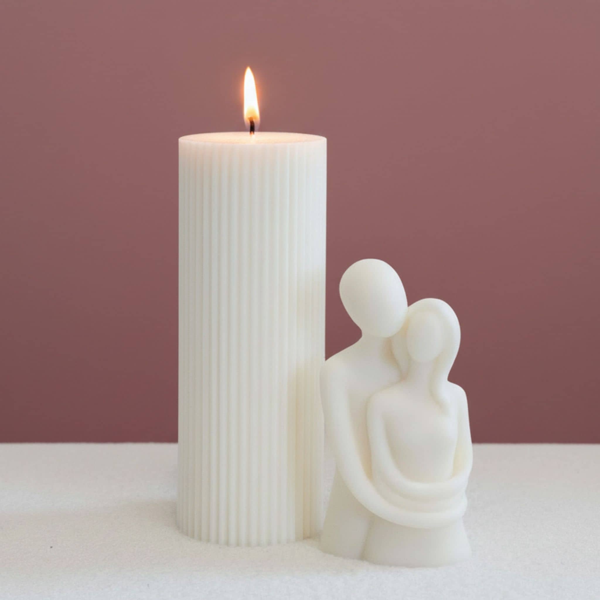 Two sculptural candles with a dark pink background and white base