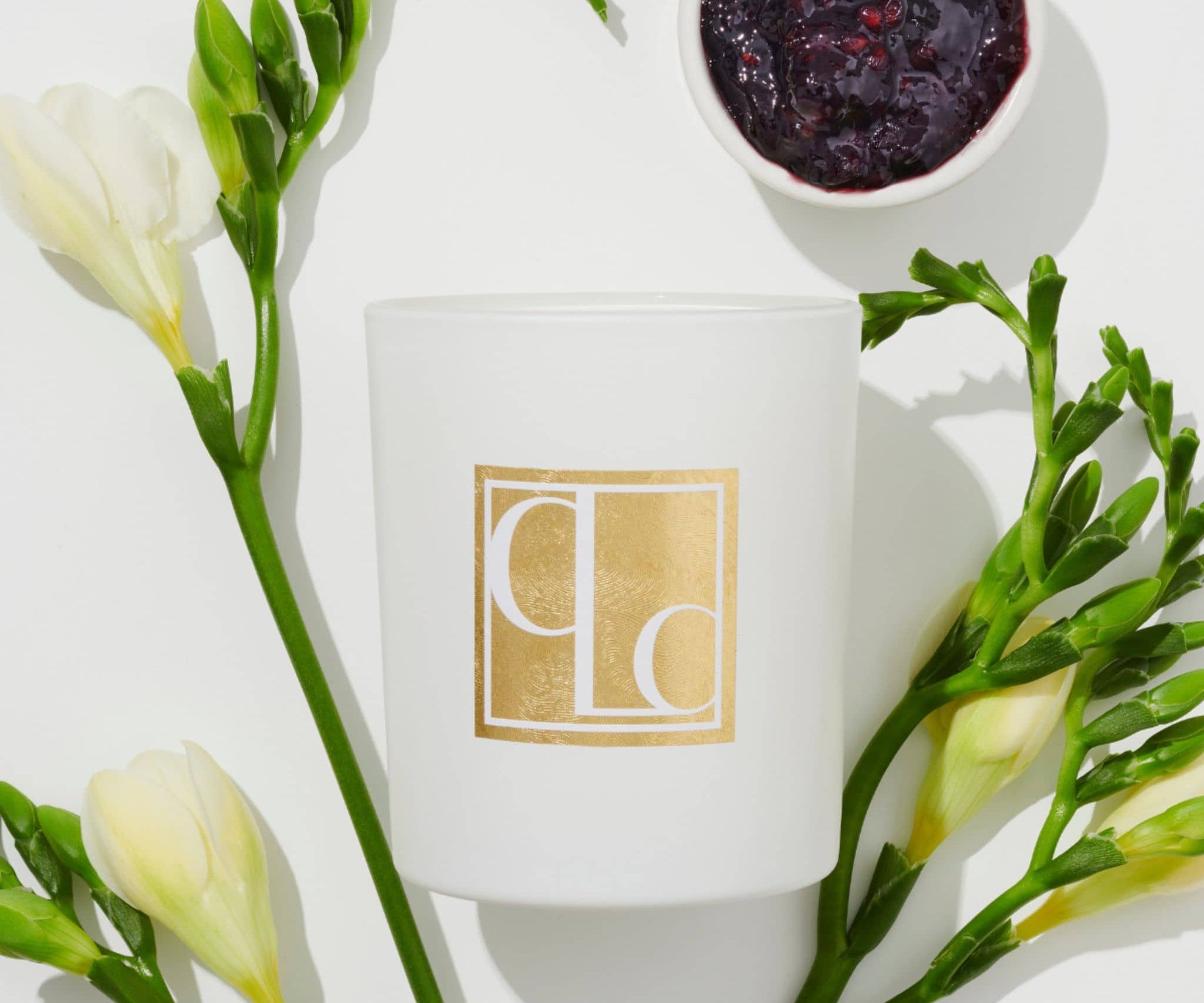 Blackcurrant and white musk scented candle flat lay with blackcurrant jam and freesias