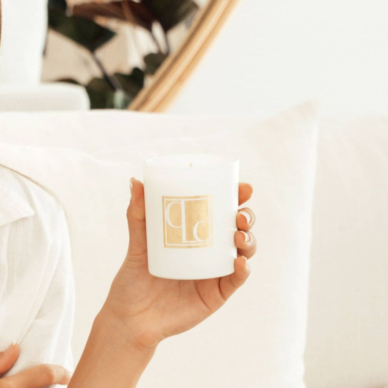Caitlin Louise Collection Signature Collection Scented Candle - held in model's hand - white lounge in background