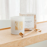 Candle labeled 'Champagne Sunset' with a decorative box and a gold wick trimer on a wooden surface.