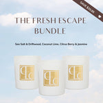 Three candles in white containers with gold logos on a light blue background with clouds.