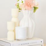 Aurelia hourglass pillar candles styled with scented candle and vase of flowers - sitting on stack of books