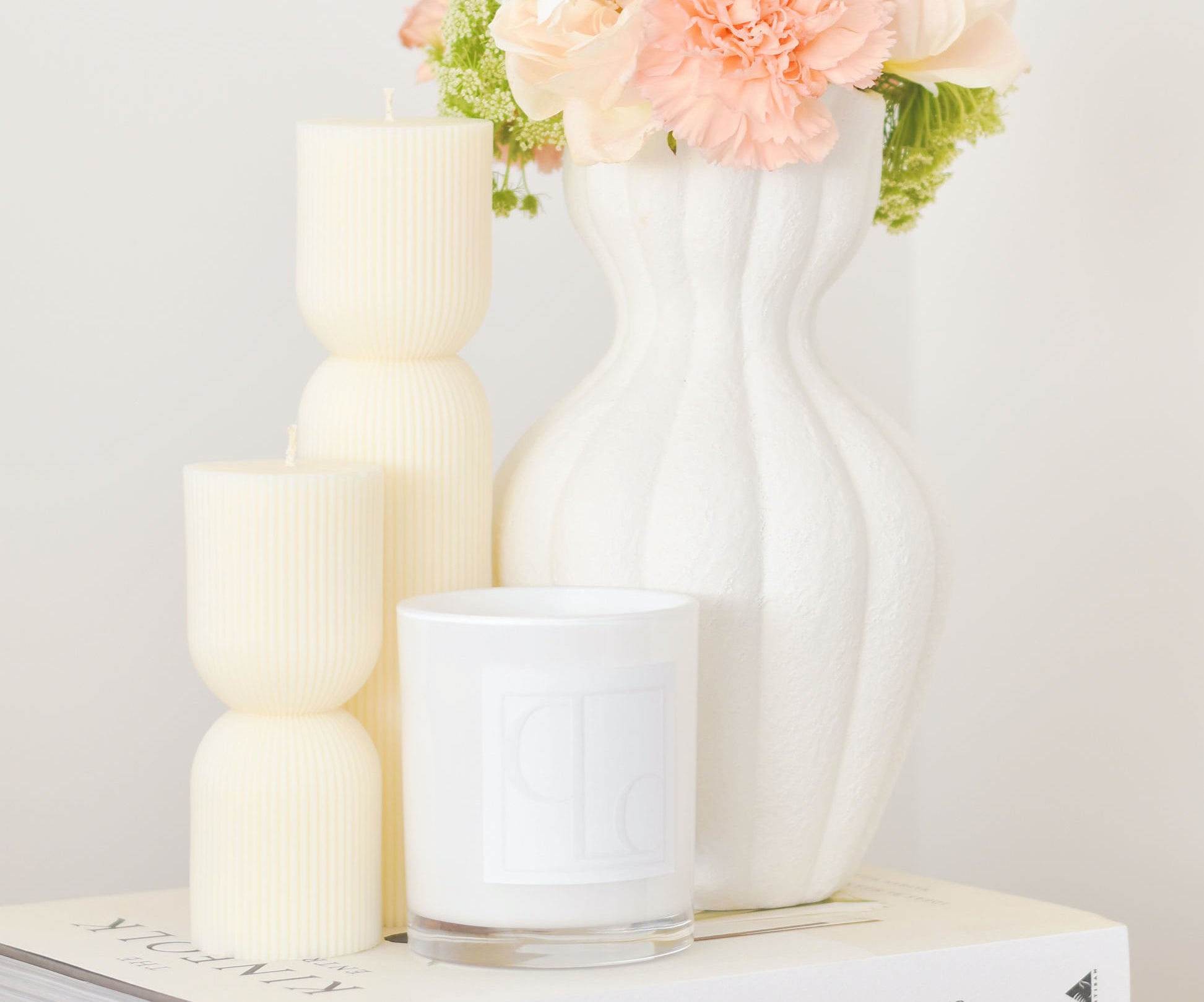 Aurelia hourglass pillar candles styled with scented candle and vase of flowers - sitting on stack of books