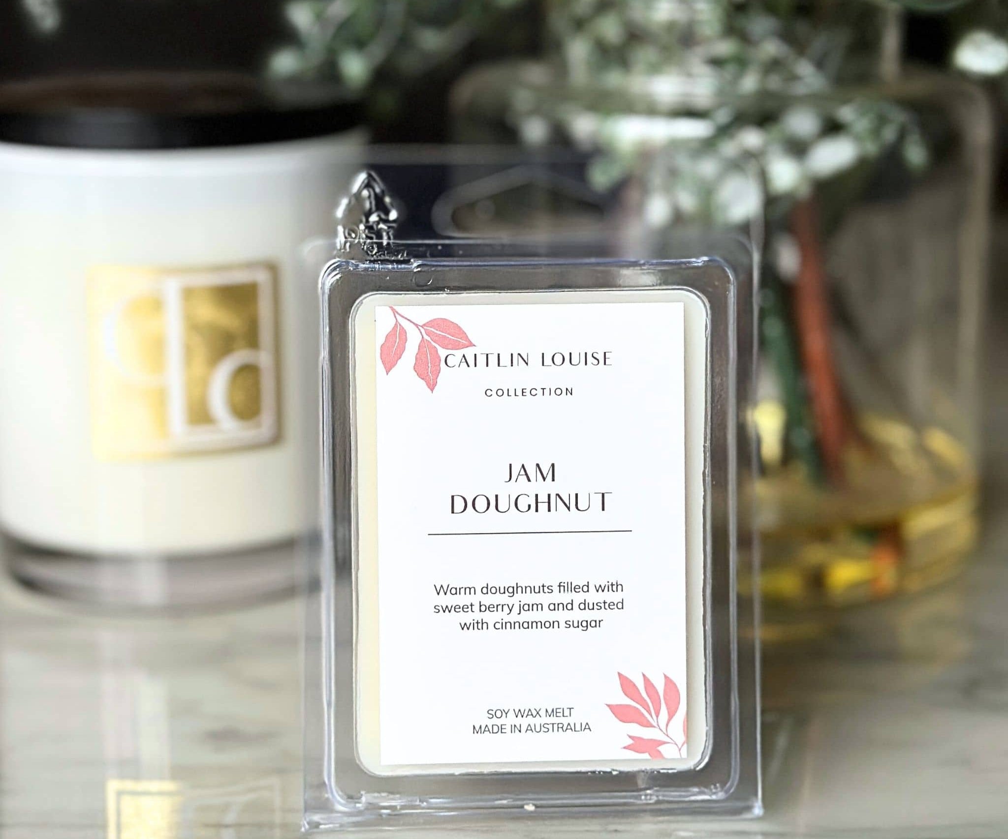 Caitlin Louise Collection wax melt labeled 'Jam Doughnut' in front of a candle.