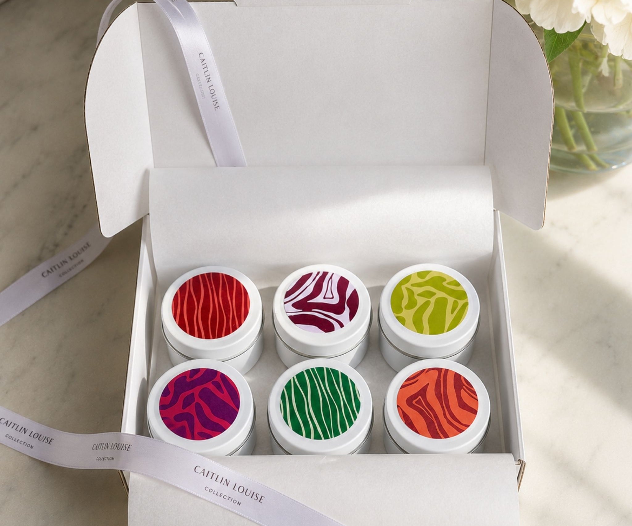 Colourful discovery set candle tins in a white box with tissue paper and ribbon
