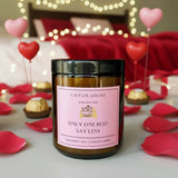 Candle with a pink label in a romantic setting with heart balloons and rose petals.