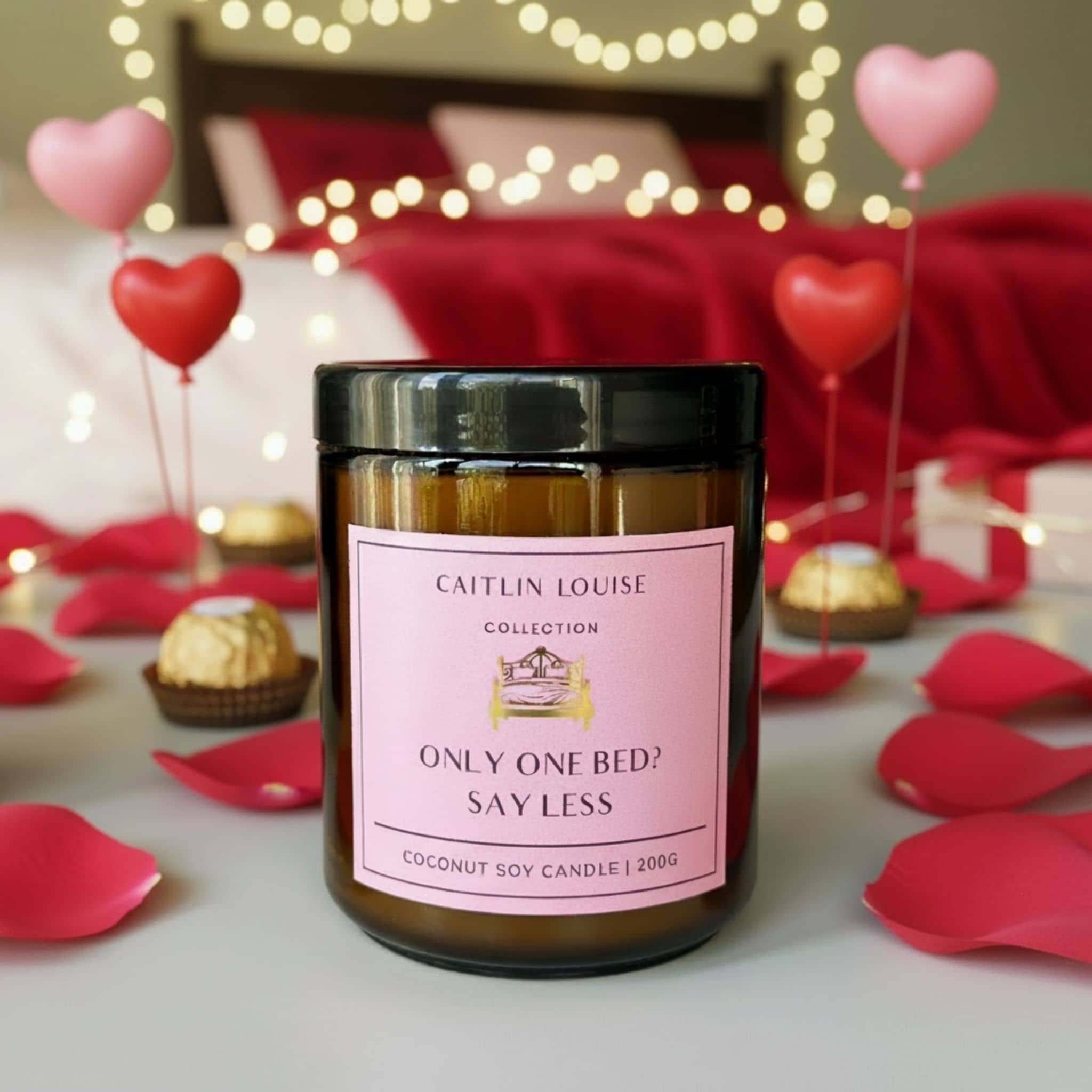 Candle with a pink label in a romantic setting with heart balloons and rose petals.