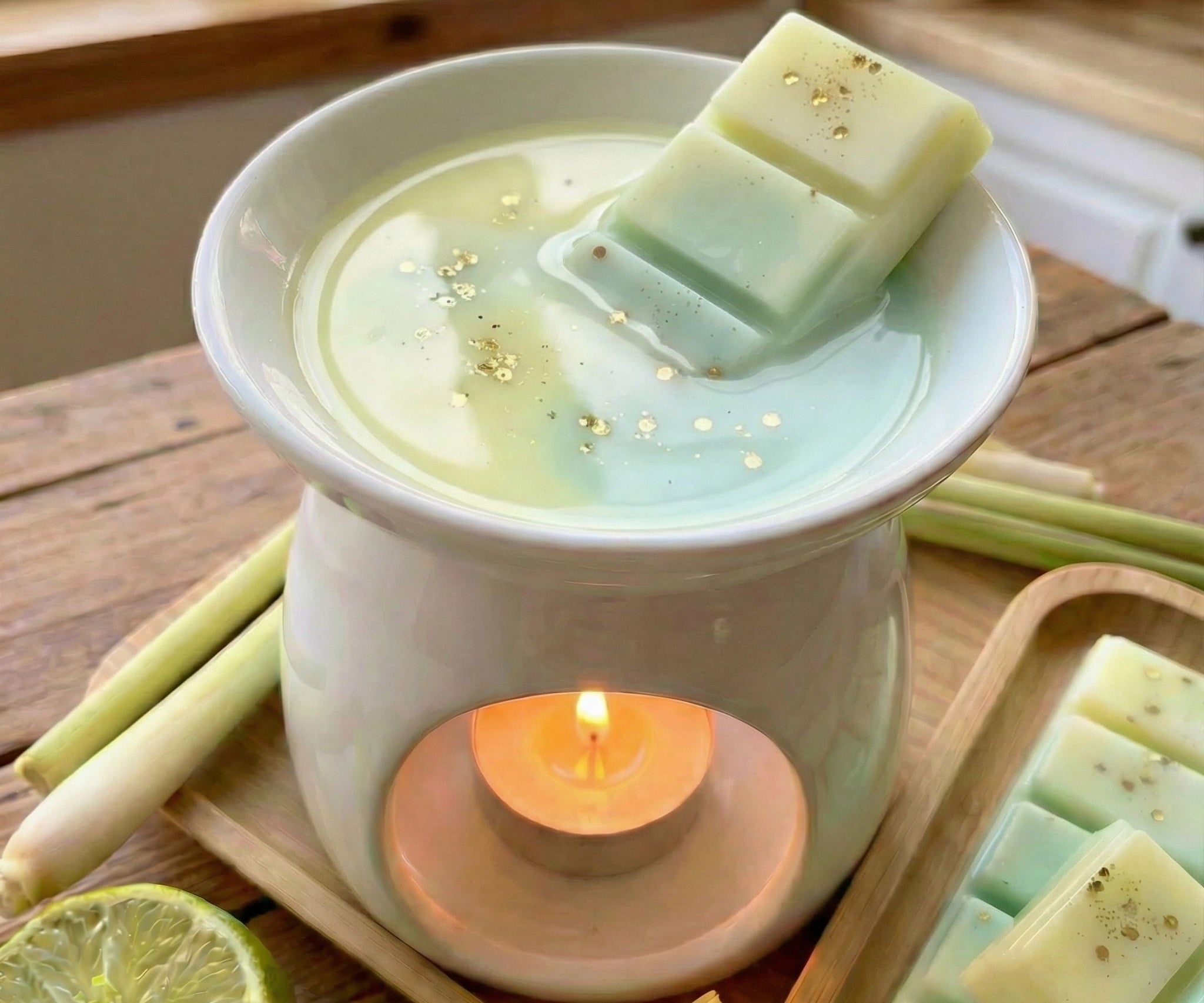 Lemongrass and lime wax melt melting in melter with ingredients surrounding it on a wooden bench