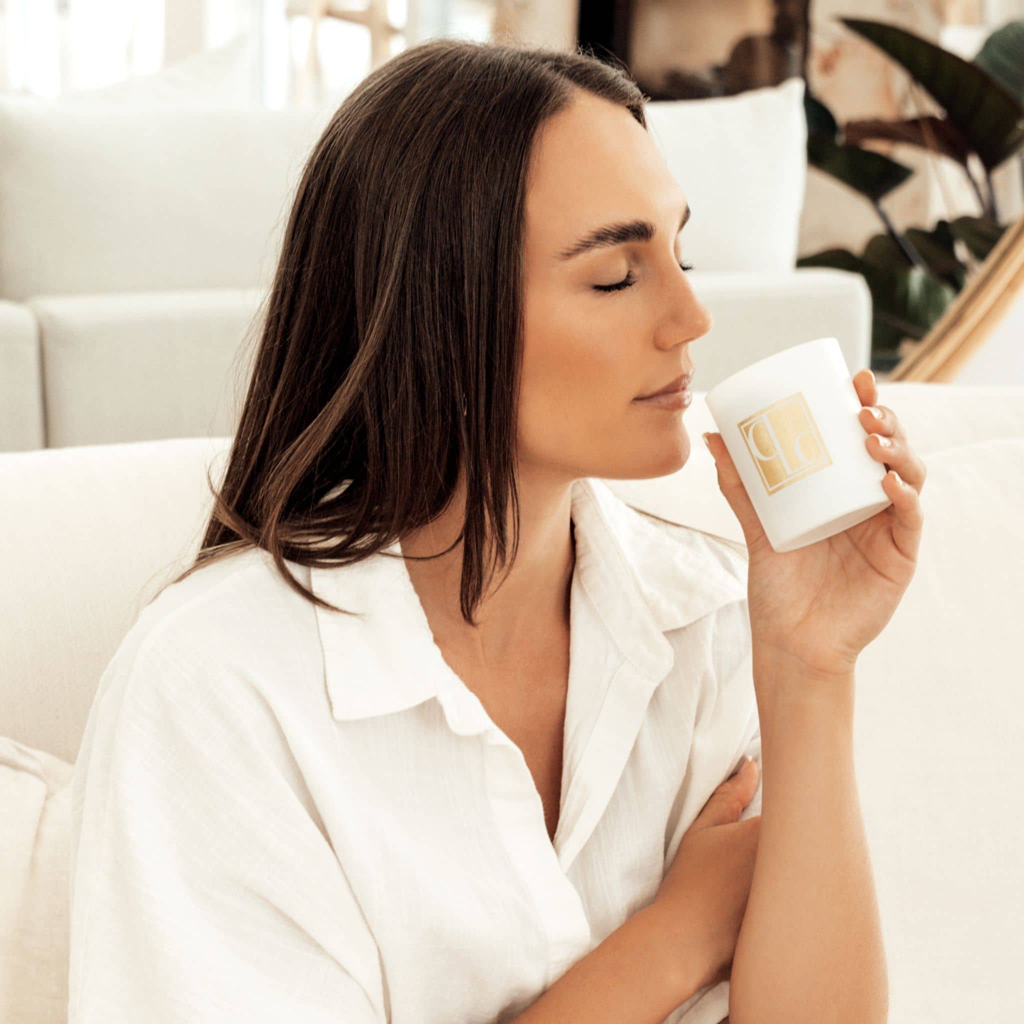 A lady sitting on a lounge smelling a Caitlin Louise Collection Signature Collection candle