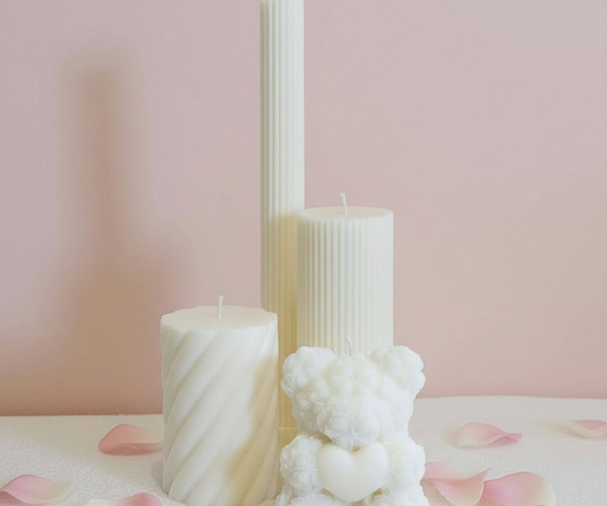 Collection of decorative candles with a light pink background and pink rose petals on the ground