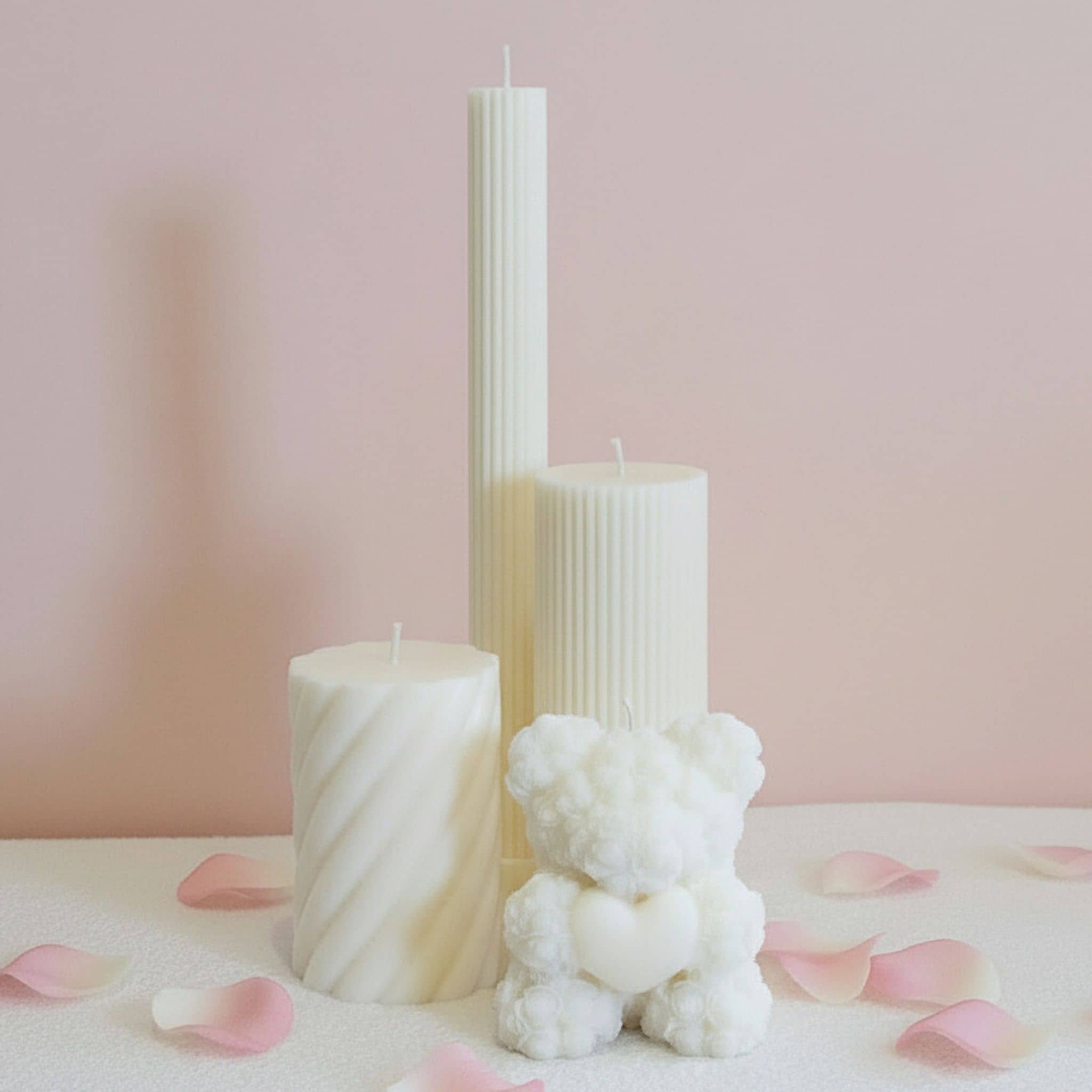 Collection of decorative candles with a light pink background and pink rose petals on the ground