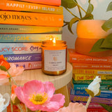 Candle titled 'A Midsummer Night' on a stack of books with flowers and a plant in the background.