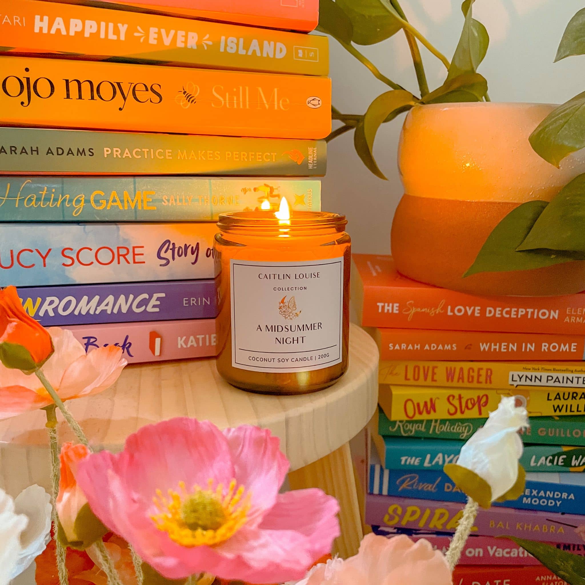 Candle titled 'A Midsummer Night' on a stack of books with flowers and a plant in the background.