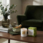 Candle and decorative items on a wooden table with a green sofa in the background