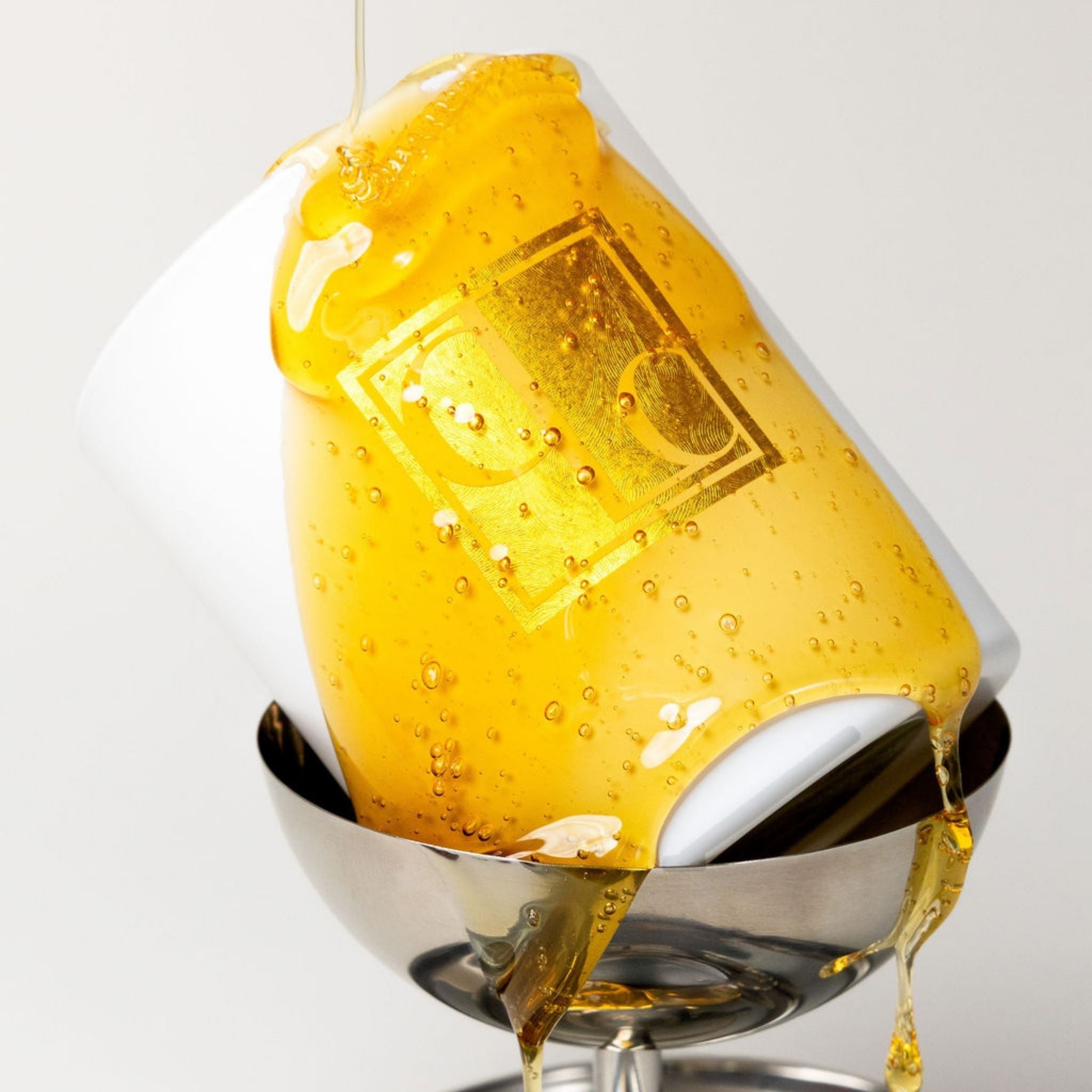 Close-up of a Caitlin Louise Collection candle drizzled with runny honey, with a focus on the bubbles.