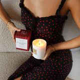 Model holding Black Cherry Woods candle in hand while sitting on lounge