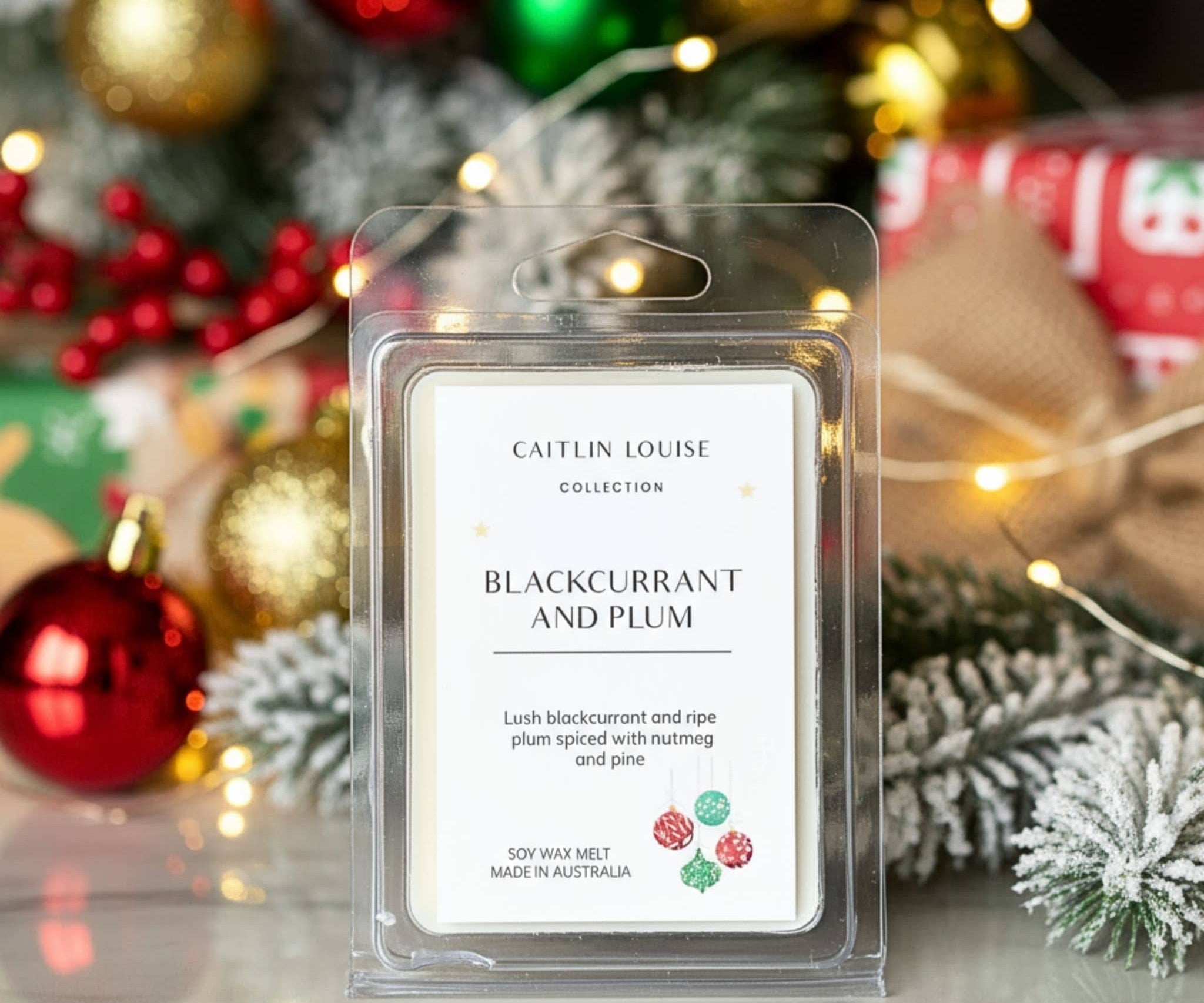 Caitlin Louise Blackcurrant and Plum wax melt packaging with Christmas decorations in the background