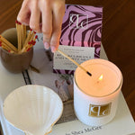 Candle being lit with a match, next to a box of matches and a book on a wooden surface.