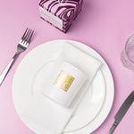Caitlin Louise Collection candle with gold logo on a white plate with cutlery on a pink background