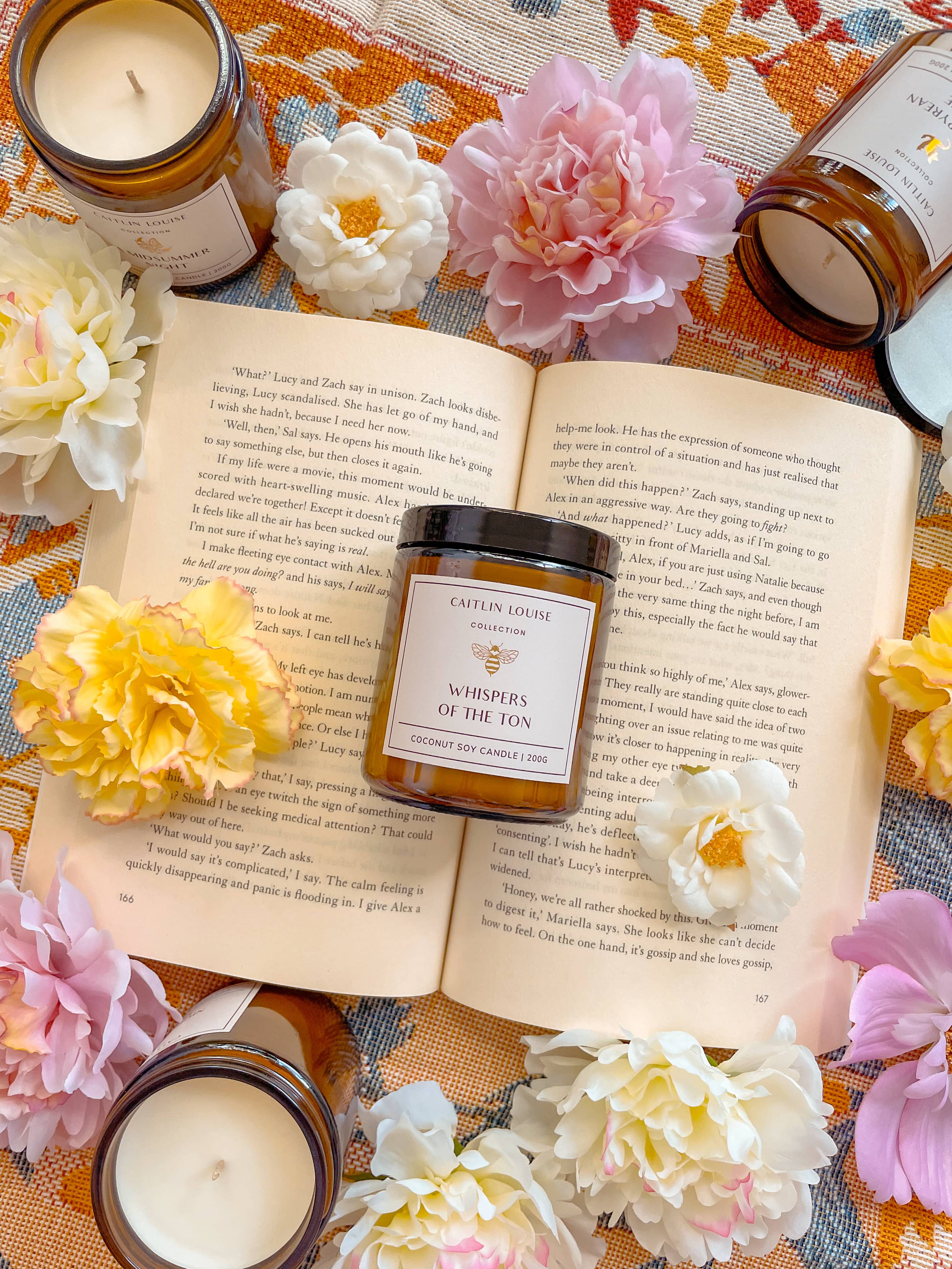 Bookish candle styled on top of open book with other candles and flowers surrounding.