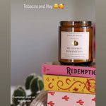 Candle labeled 'My Cowboy Romance Era' on a stack of books with a cactus in the background