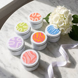Set of small discovery set candle tins with colourful lids on a marble surface with a white flower.