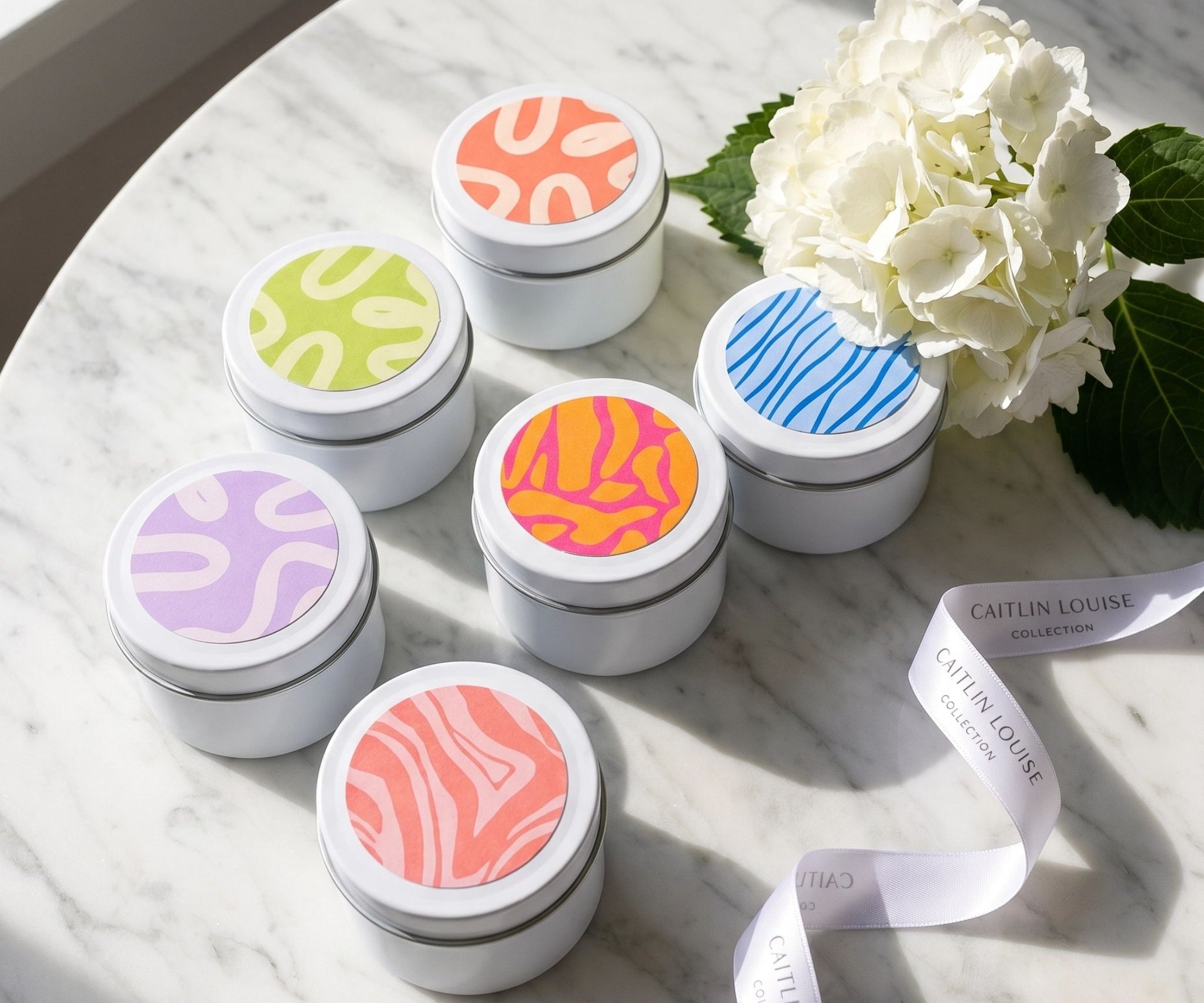 Set of small discovery set candle tins with colourful lids on a marble surface with a white flower.
