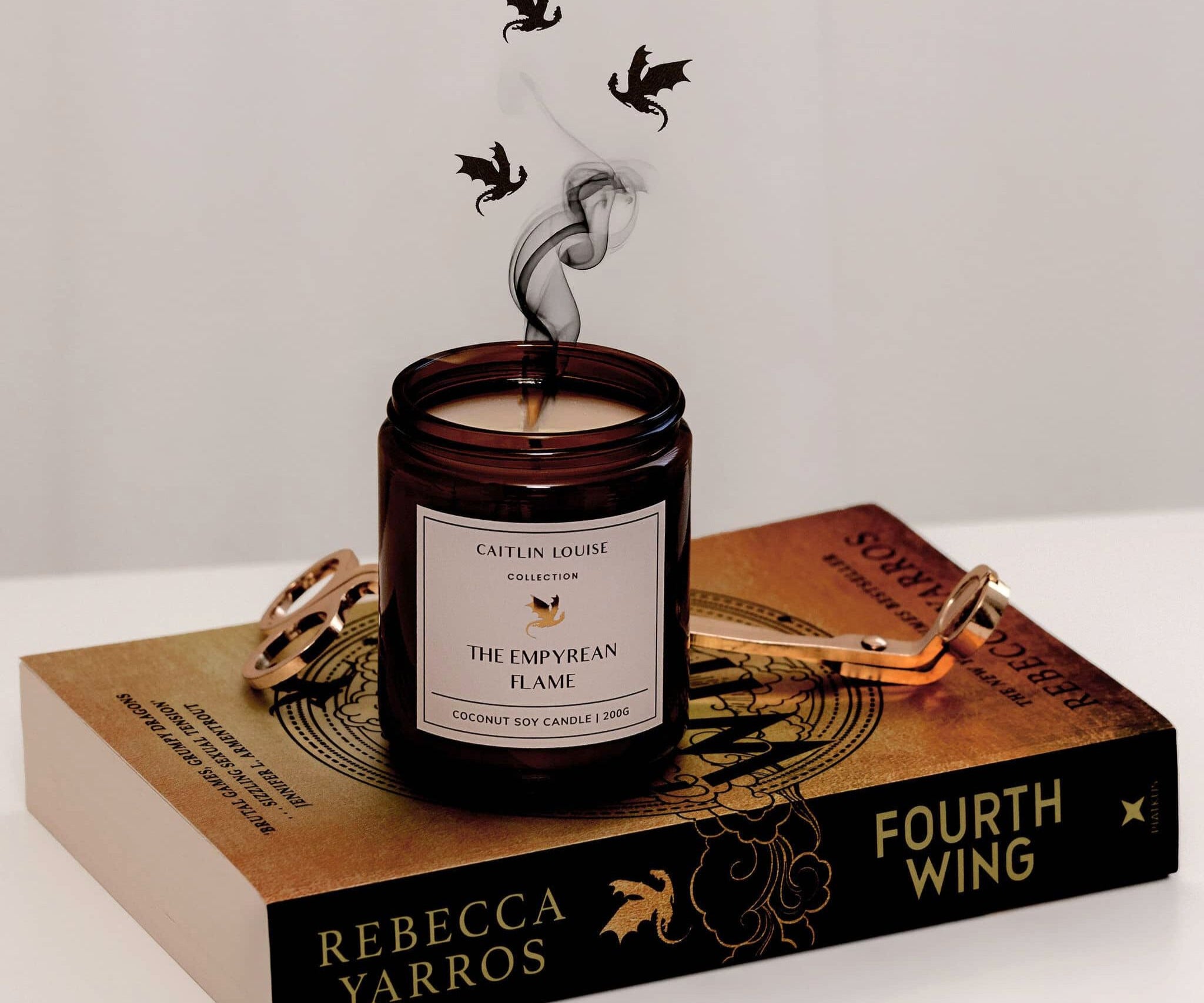 Caitlin Louise Collection The Empyrean Flame Bookish Candle - sitting on Fourth Wing book with dragons flying around smoke from the wick