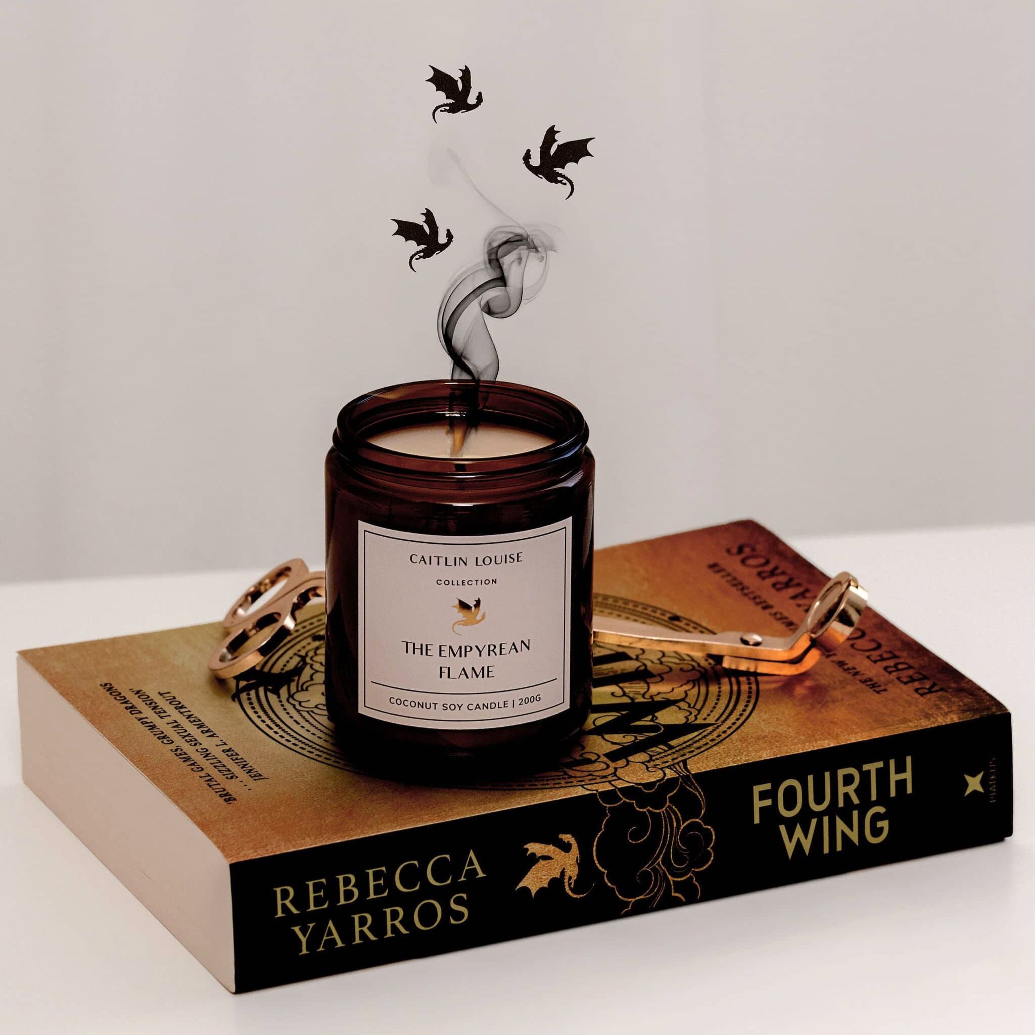 Caitlin Louise Collection The Empyrean Flame Bookish Candle - sitting on Fourth Wing book with dragons flying around smoke from the wick