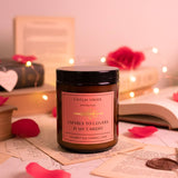 Candle with a pink label on a surface with books and heart-shaped objects