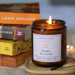 Candle in an amber jar with a label on a wooden coaster, books in the background