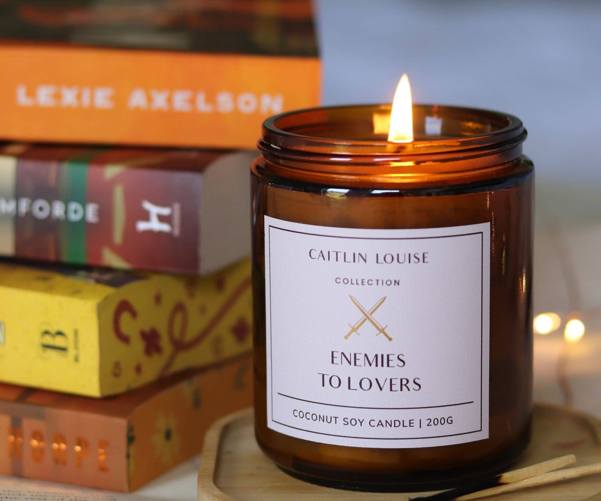 Candle in an amber jar with a label on a wooden coaster, books in the background