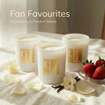 Three Caitlin Louise Collection candles on a light surface with strawberries and flowers.