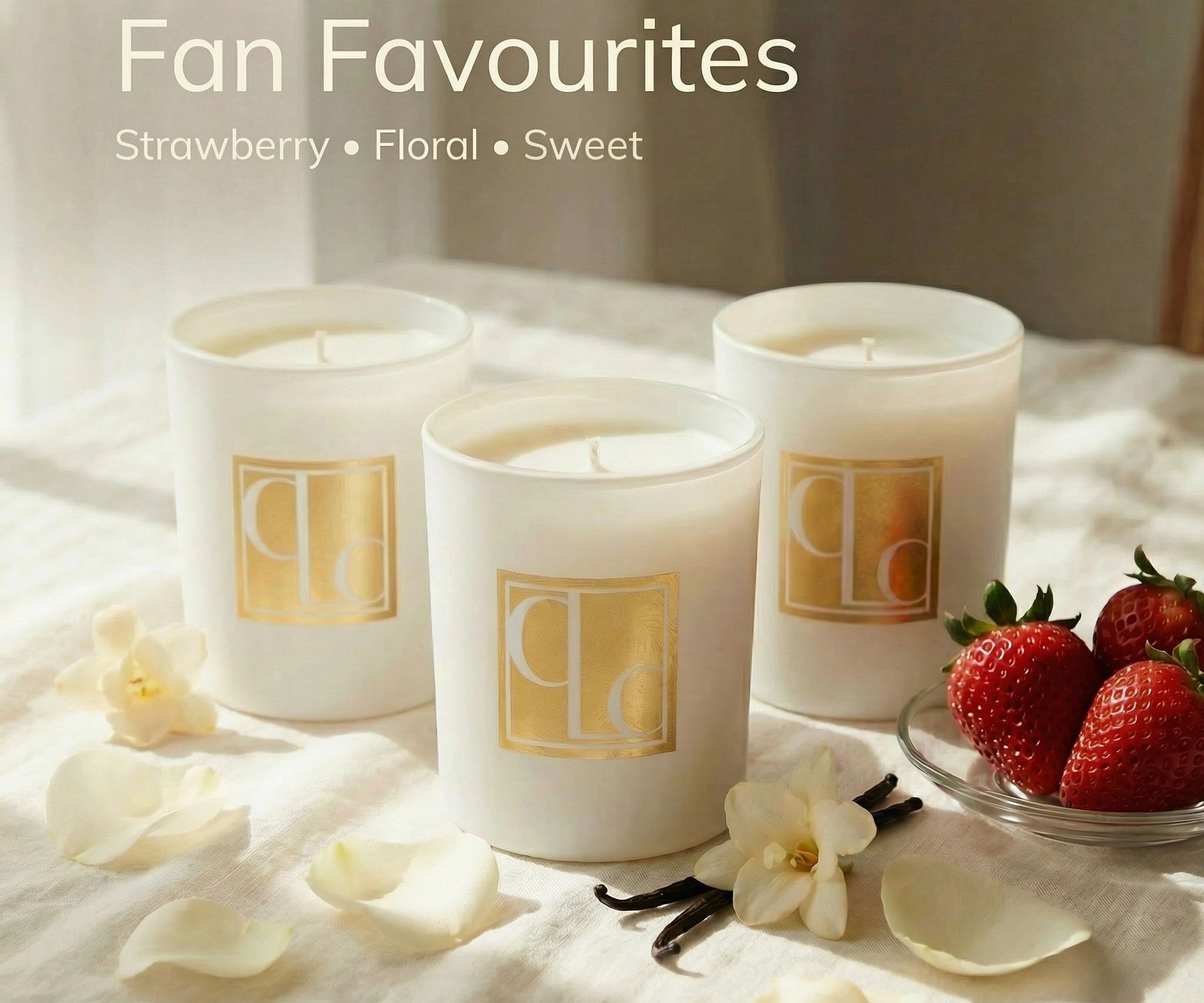 Three Caitlin Louise Collection candles on a light surface with strawberries and flowers.