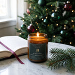 Christmas bookish candle on marble table with open book nearby and christmas tree background