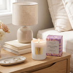 Candle, books, and a lamp on a wooden surface next to a bed.