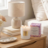 Candle, books, and a lamp on a wooden surface next to a bed.