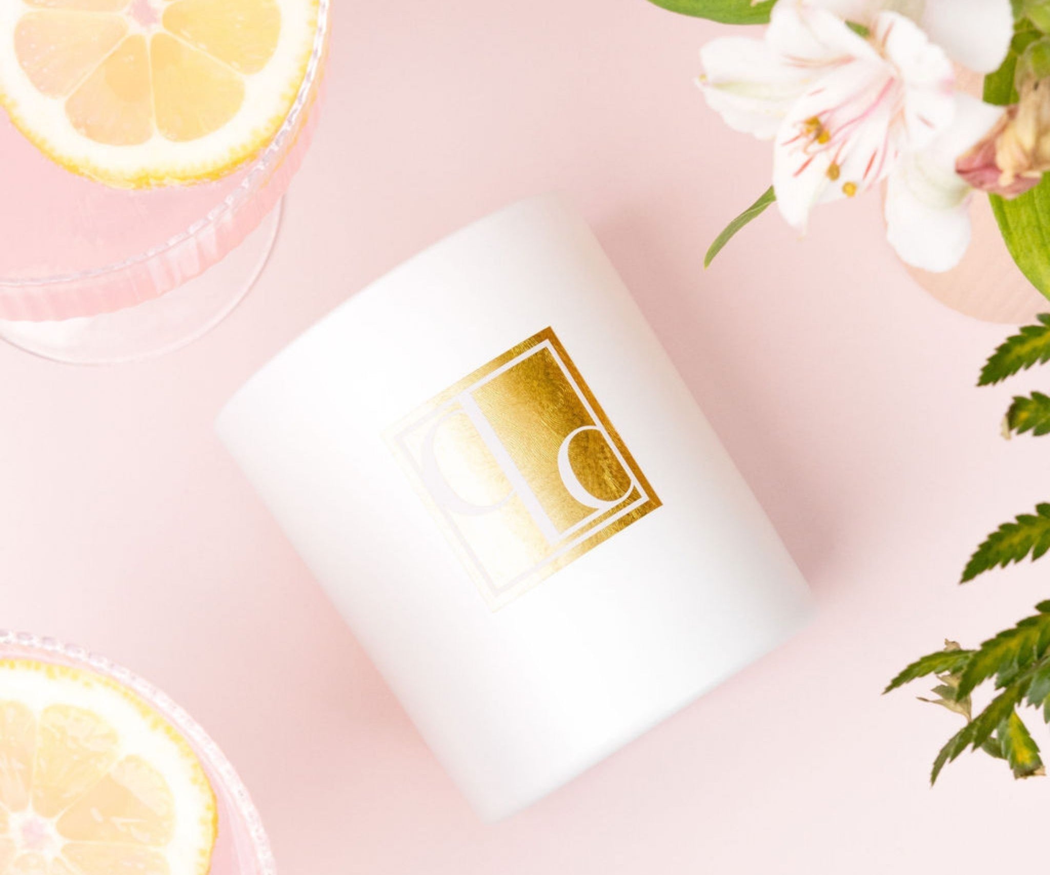 Caitlin Louise Collection white candle with gold logo on a pink background with lemon slices and flowers
