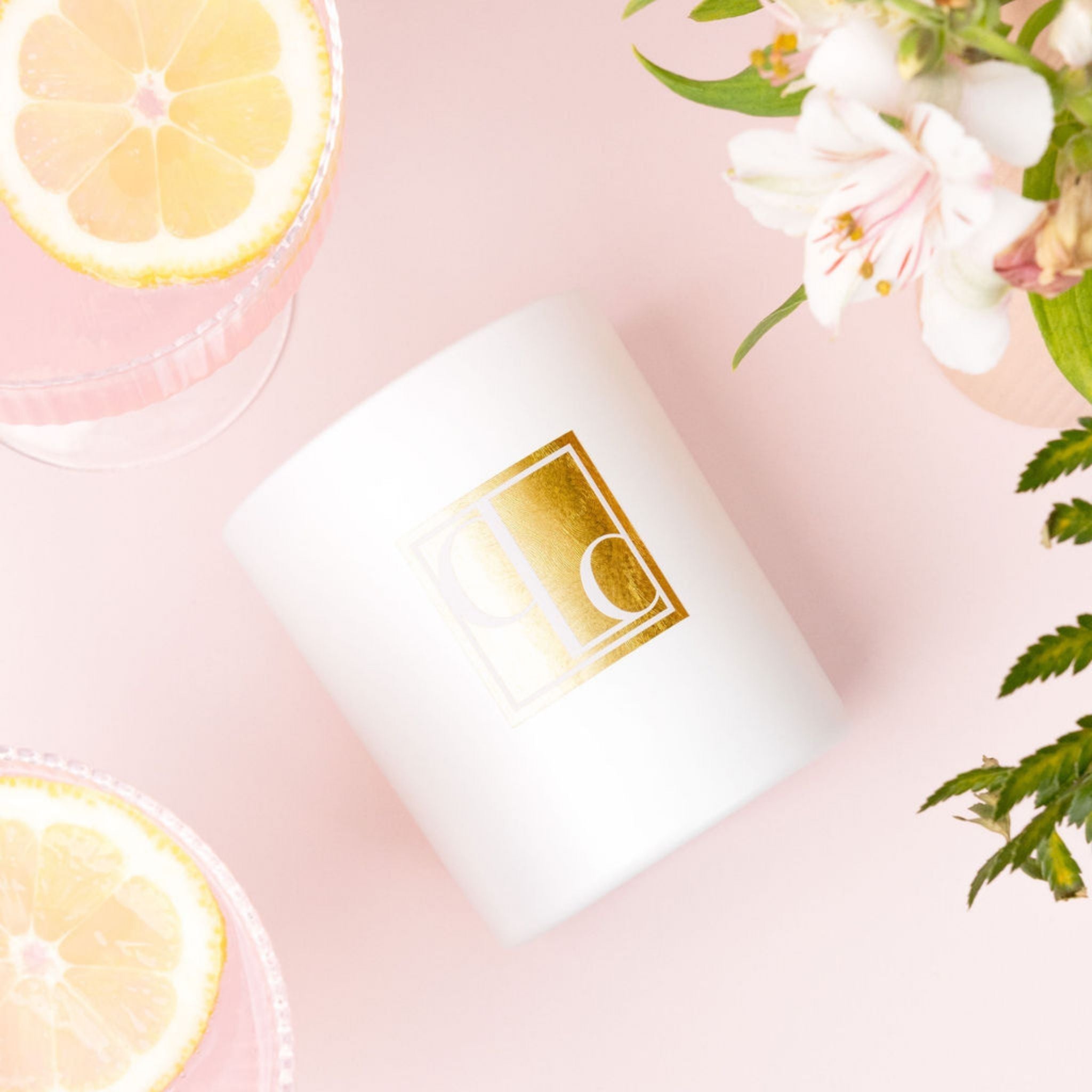 Caitlin Louise Collection white candle with gold logo on a pink background with lemon slices and flowers