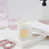 Caitlin Louise Collection Japanese Honeysuckle scented candle on a tray surrounded by light pink scrunchies, hand towel, pink glass filled with water and hand pump - bathroom scene.